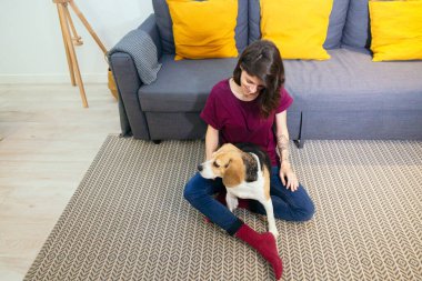 Bir kadın oturma odasında köpeğini okşuyor.