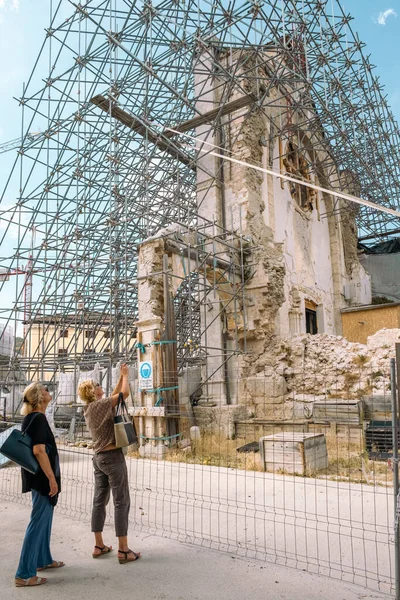 2人の人が2016年の地震で破壊された教会を見ています。イタリアのノルチャ ロイヤリティフリーのストック写真