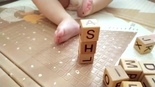 Девочка сидит на полу и играет с деревянными кубиками с английскими буквами — стоковое видео