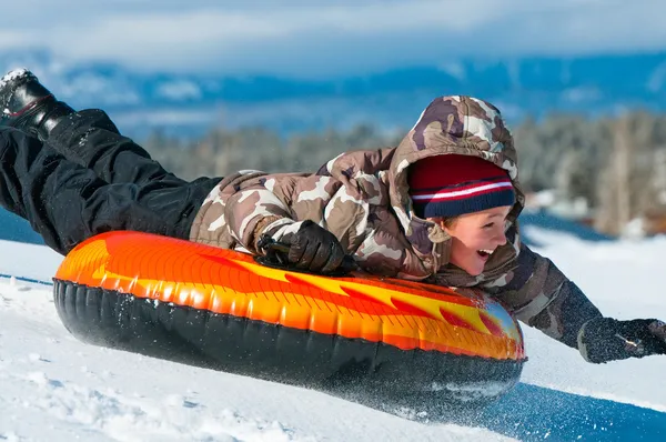 Glücklicher Junge, der eine Röhre im Schnee reitet — Stockfoto