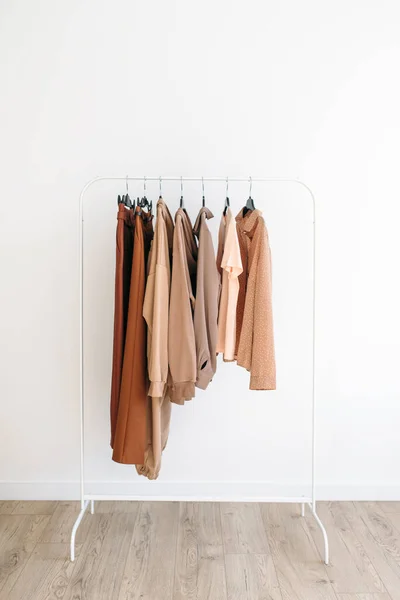 Beige capsule of clothes on a rack over white background