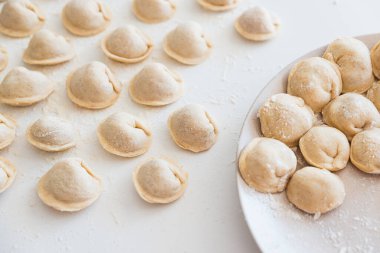 Beyaz masada pişmemiş ev yapımı pelmeni. Pelmeni, ravioli veya etli hamur tatlısı yapma süreci