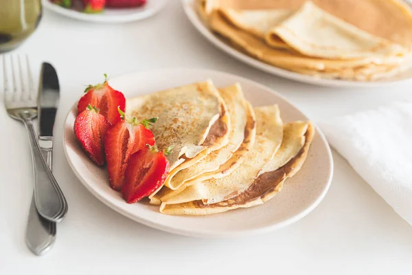 French crepes with chocolate spread and strawberries on white table