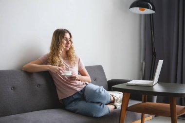 Kanepede beyaz bir fincan kahveyle oturan güzel genç bir kadın, beyaz dizüstü bilgisayarla çalışıyor. Pembe gömlekli kız monitöre bakıyor. Uzaklık öğrenme öğrencisi