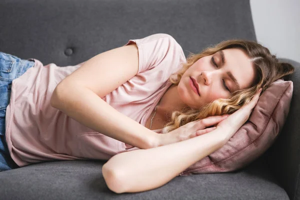 Gri kanepede uyuyan güzel bir genç kadın. İşten sonra pembe gömlekli kız evde dinleniyor..