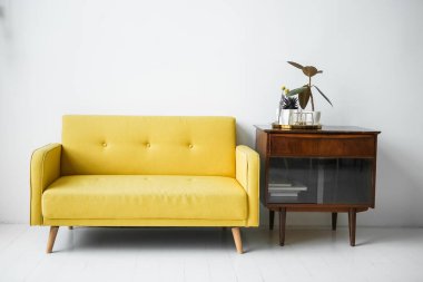 Beyaz bir zeminde sarı bir kanepe ve ahşap bir sehpa ile beyaz bir duvara karşı şık bir oda. Minimalist iç mekan