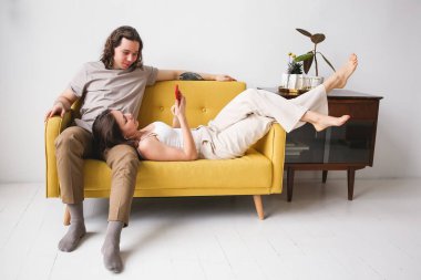 Telefona bakan bir çift. Bir adam ve bir kadın akıllı telefonuyla kanepede yatıyor. Uzak servislerin kullanımı