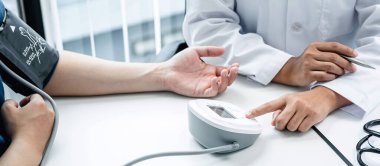 Doktor, kan basıncını ölçmek için kan basıncı monitörüne basın. Doktor, kan basıncı verilerini kaydetmek ve hastanın semptomlarını kaydetmek için kalemi tutun.
