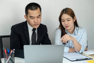 Takım elbiseli işadamı patron ona yeni iş projesini anlatıyor ve kadın ofis çalışanı da ofiste birlikte çalışırken bilgisayardan iş verilerine bakıyor.