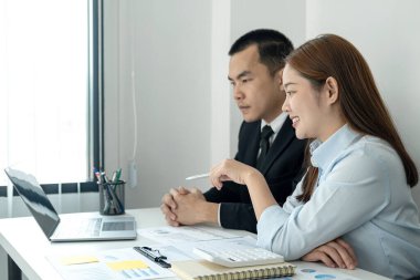 Takım elbiseli işadamı patron ona yeni iş projesini anlatıyor ve kadın ofis çalışanı da ofiste birlikte çalışırken bilgisayardan iş verilerine bakıyor.