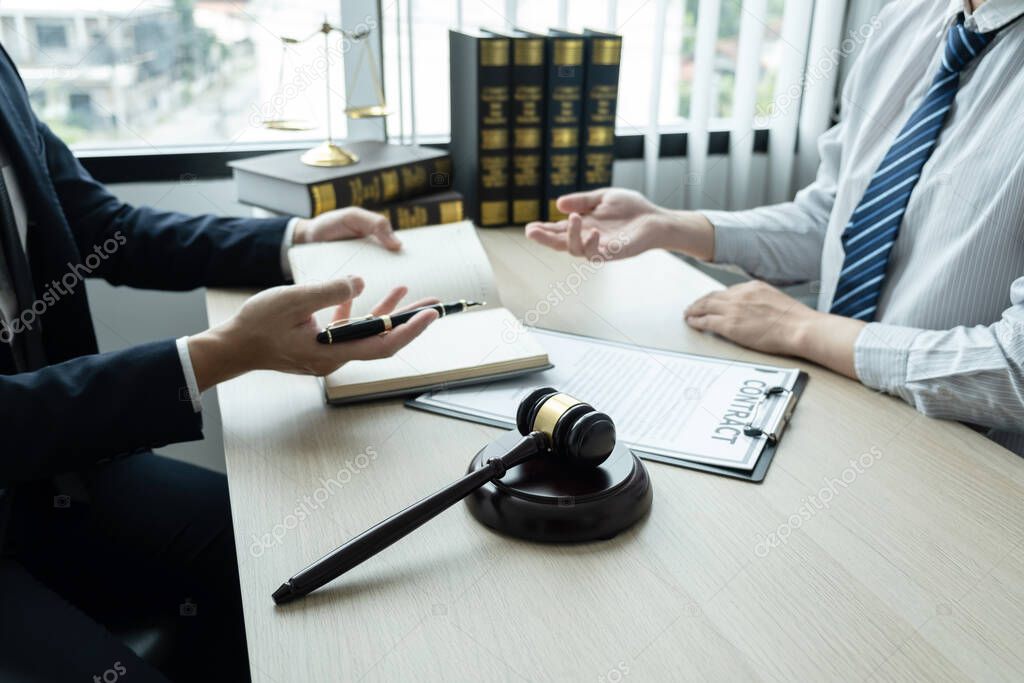 Male lawyer working on documents contract papers of the important case with the business customer and wooden gavel, brass scale in office.