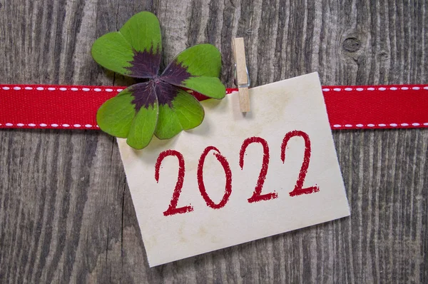 Wooden hang tag and slate with four leaf clover and sparklers with happy new year 2022 on wooden weathered background