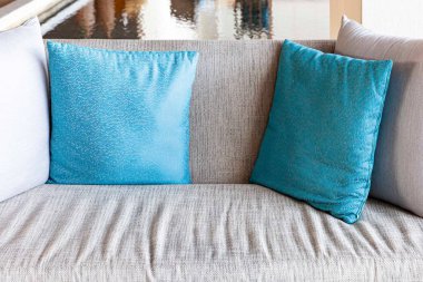 Modern bir oturma odasındaki gri kumaşlı, uzun koltukta mavi ve gri yastıklar.