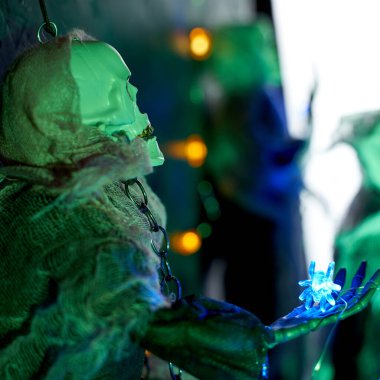 Karanlık bir arka planda bir iskeletin kolunda parlayan örümceklerden oluşan Cadılar Bayramı süsleri.