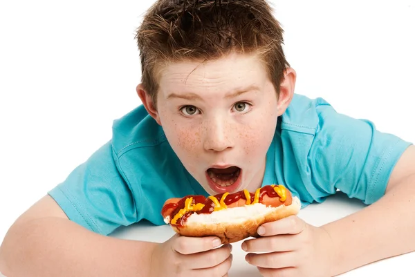 Éhes fiatal fiú eszik a hotdog. — Stock Fotó
