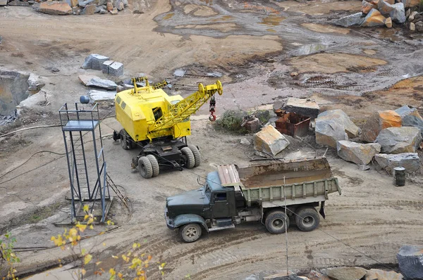 Granit ocağında eski paslı boş bir kamyon, sarı vinç ve aydınlatma kulesi taşların arasında.