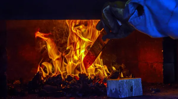 プロの鍛冶職人は 金属片を石炭鍛造品の踊りの炎に慎重にそして熱心にスライドさせます 金属はすぐにカスタムメイドのナイフになります — ストック写真