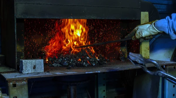 保護革の手袋を着用し 鍛冶屋は石炭フォージ内の炎を攪拌するためにポーカーを使用していますカラフルな火花が周りを飛ぶ ぼっけ — ストック写真
