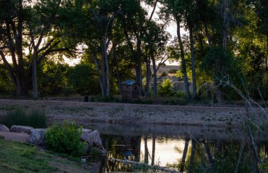 Colorado 'da güzel bir kır manzarası. Bir gölet, bir yol ve ağaçların arasına yerleştirilmiş eski moda ahşap bir ek bina. Arka planda küçük yuvarlanan dağlar var..