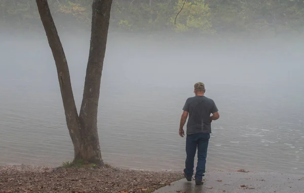 Fog hangs over the river on a cool morning in Arkansas. This man who can not be identified walks along the banks to do a little sightseeing. Bokeh.