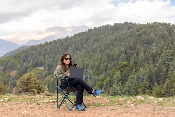 Woman working with her computer in nature, working with a computer in the forest.