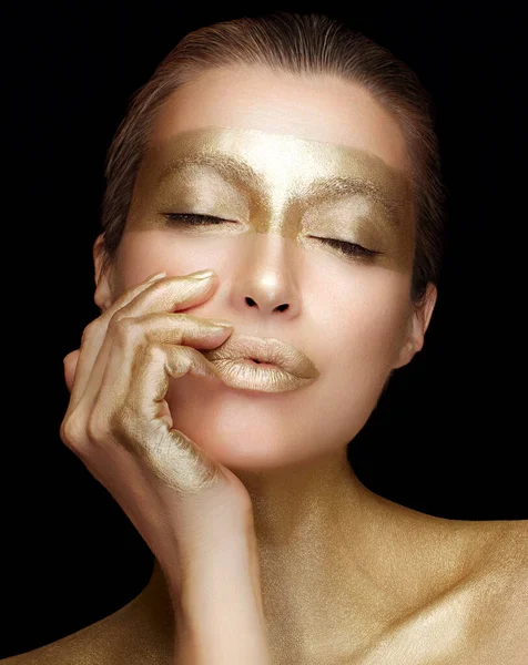 Beauty and makeup concept. High Fashion model girl with golden cosmetics on a glowing skin. Art make-up in metallic gold, golden lips and gold make up. Close-up portrait isolated on black background