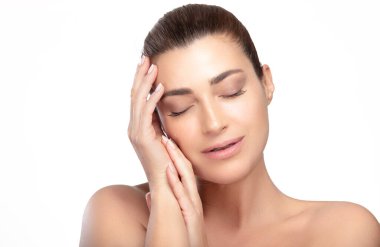 Skin Care Makeup Concept. Natural beauty with perfect skin tone and glowing hydrated makeup. Model woman with natural makeup posing with eyes closed and hands raised gracefully to her cheek