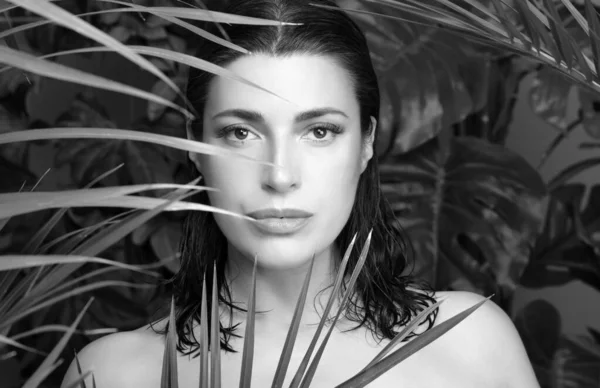 Organic beauty and skin care concept. Beautiful woman with flawless skin and wet hair amongst tropical plants. Monochrome portrait in horizontal format