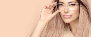 Stüdyoda poz veren güzel, berrak çerçeveli bir kadın yüzü. Çıplak makyajlı güzel bir kadın bej arka planda gözlük takıyor. Moda gözlüğü ve açık görüş konsepti