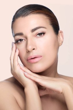 Güzellik ve makyaj konsepti. Kusursuz çıplak makyaj temeli olan manken kız. Kusursuz cilt ve manikürlü tırnaklara uyan çıplak ruj. Bej arka planda dikey yüksek moda portresi