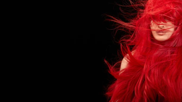 Dyed hair care and fashion concept. Fashion model girl with windswept long dyed red hair. Beautiful red haired woman with shiny long flying hair. Isolated on black with copy space