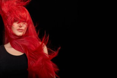 Red haired woman with a beautiful and healthy long red hair. Flying hair isolated on black background with copy space
