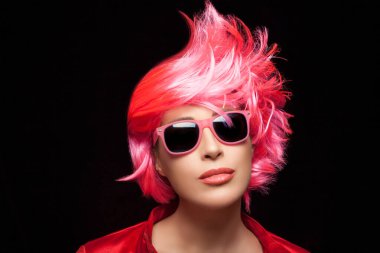 Fashionable woman with stylish dyed pink hair and trendy colorful sunglasses isolated on black background with copy space