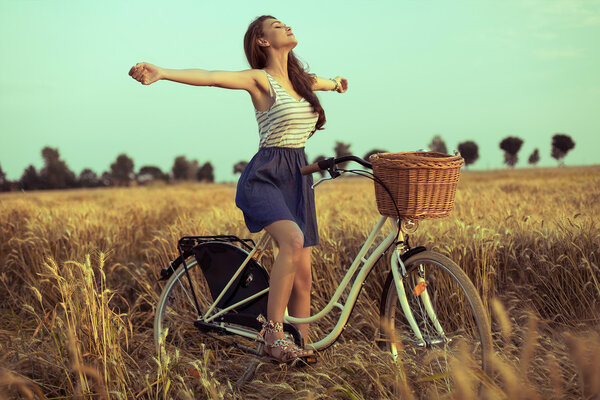 Free woman enjoying freedom on bike on wheat field at sunset