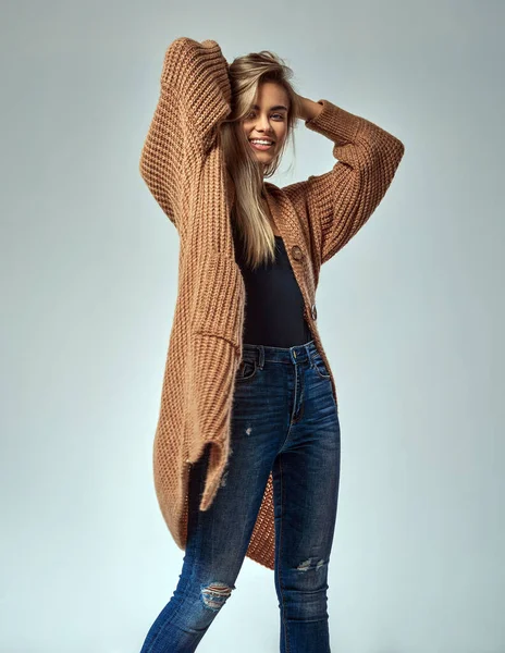 Güzel genç bir kadın şık kıyafetler giyer. Sarışın güzel, gri arka planda mavi kot pantolon ve yün süveter giyiyor.