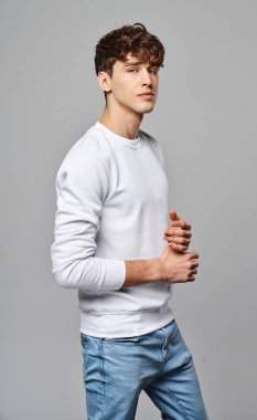 Gri arka planda beyaz kazaklı genç adam. 