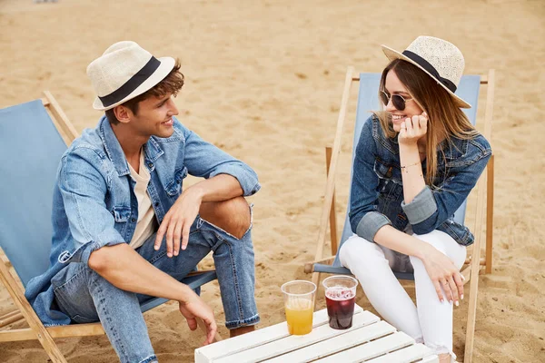 一对年轻貌美的年轻夫妇坐在海滩椅子上喝着果汁 一对年轻夫妇在户外恋爱的画像 — 图库照片