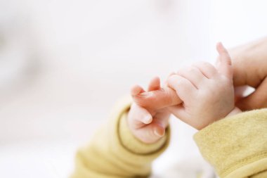 Annenin parmağını tutan Asyalı bebek.