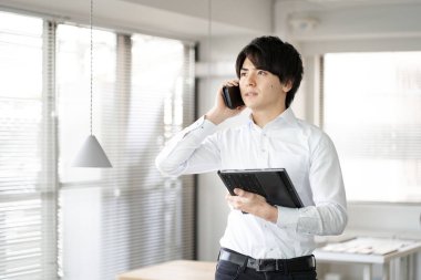 Asyalı adam ofiste telefon görüşmesi yapıyor.