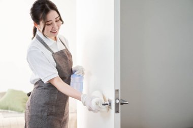 Asyalı kadın kapı kollarını alkolle sterilize ediyor.
