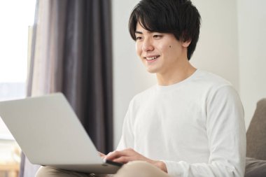 Asyalı adam oturma odasında bilgisayar kullanıyor.