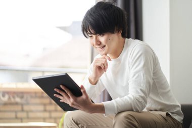 Asyalı adam oturma odasında tablet kullanıyor.