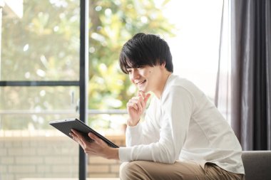 Asyalı adam oturma odasında tablet kullanıyor.