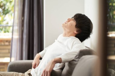 Asyalı adam oturma odasında dinleniyor.