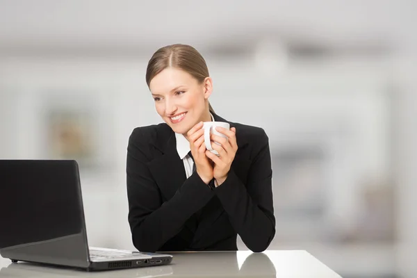Mujer de negocios sonriente sentada con computadora portátil, sosteniendo taza de café y té —  Fotos de Stock
