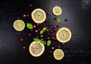 Siyah ahşap bir masada limon, kızılcık ve nane.