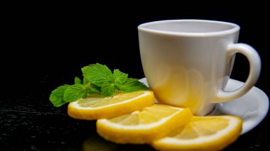 Siyah arka planda çay olan beyaz bardak. Bir fincan tabağında limon dilimleri. Yakın plan..