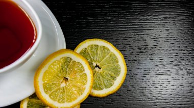Siyah arka planda çay olan beyaz bardak. Bir fincan tabağında limon dilimleri. Boşluğu kopyala.