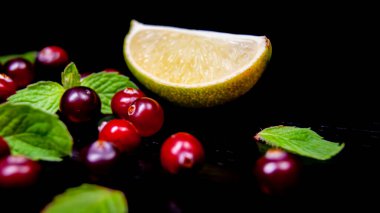 Siyah ahşap bir masada, nane filizi ve kızılcıklı limon dilimi.