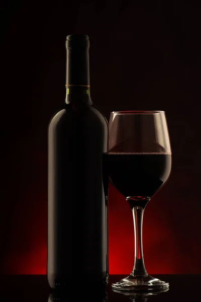 Bardağı dolu kırmızı bir şarap şişesi.